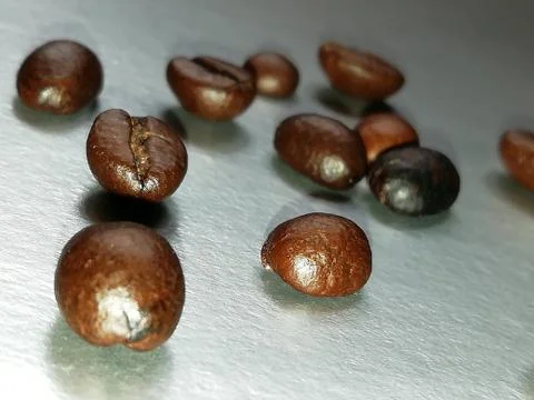 Roasted coffee beans on a silver surface. Ingredient for morning coffee. Stock Photos