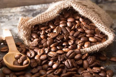 Roasted coffee beans in small sack on metal surface Stock Photos