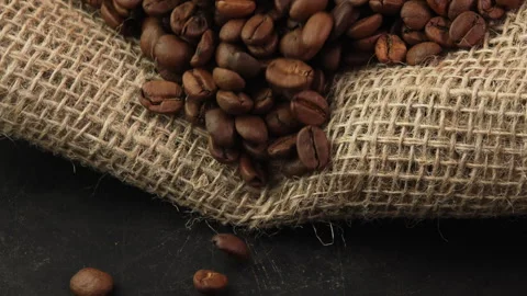 Roasted coffee beans spill out of a burlap sack onto a dark surface. Coffee Stock Footage 308323443