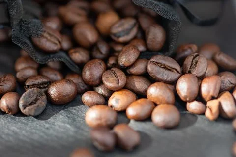Roasted coffee beans spilling from a black cloth bag Фото