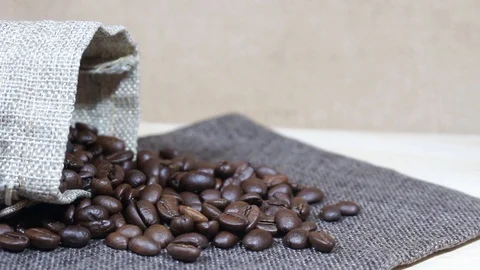 Roasted coffee beans tumbling down into pile of coffee beans next to burlap sack Stock Footage 95808803