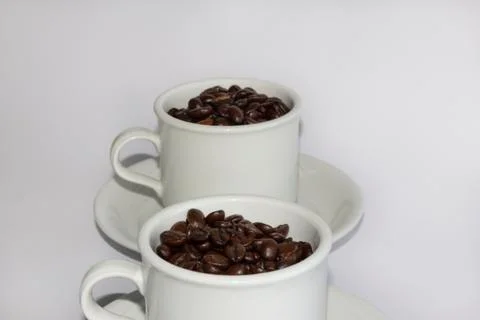 Roasted coffee beans in two coffee cups , on white isolated background. Stock Photos
