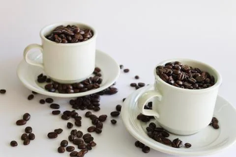 Roasted coffee beans in two coffee cups , on white isolated background. Stock Photos