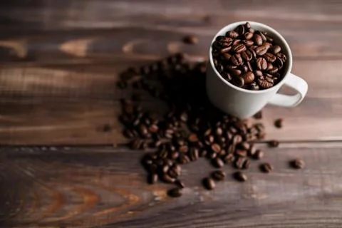 Roasted coffee beans in white cup at wood background Stock Photos