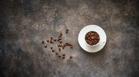 Roasted coffee beans in white cup on stone textured background with copy spac Stock Photos