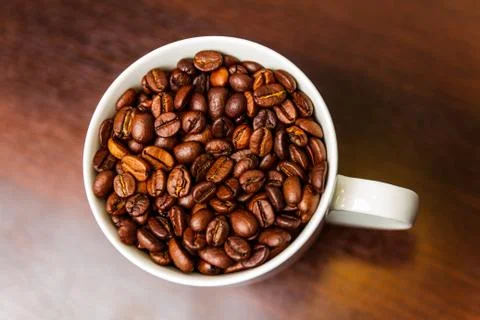 Roasted Coffee beans in a white mug cup isolated on a rustic wood table 스톡 사진