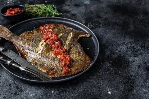 Roasted Flatfish or Flounder in a tomato sauce. Black background. Top view. Copy Stock Photos