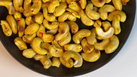 Roasted golden cashew nuts on black presentation plate, top view Stock Footage 336471085
