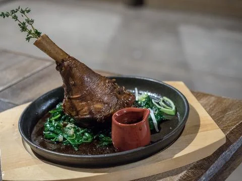 Roasted lamb knuckle served with fried spinach and thymus on rustic metal pan Stock Photos