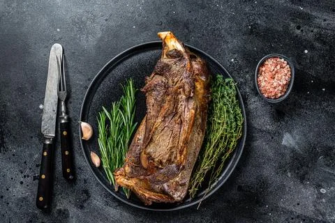 Roasted lamb mutton shoulder meat on a plate with knife and fork. Black Stock Photos