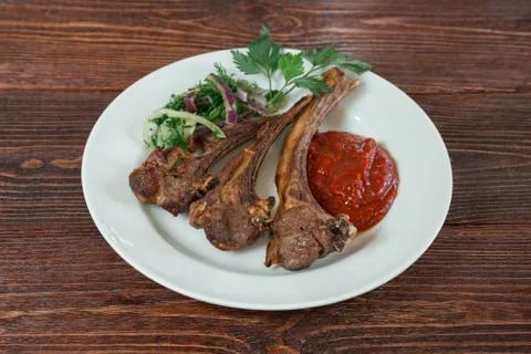 Roasted lamb ribs on a plate. Appetizing dish on the wooden brown table. Stock Photos