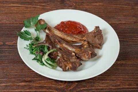 Roasted lamb ribs on a plate. Appetizing dish on the wooden brown table. Stock Photos