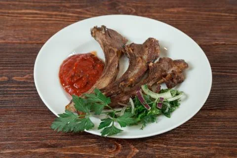 Roasted lamb ribs on a plate. Appetizing dish on the wooden brown table. Stock Photos