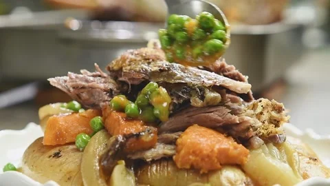 Roasted lamb shoulder with vegetables. The cook adds green peas. Stock Footage 195531250