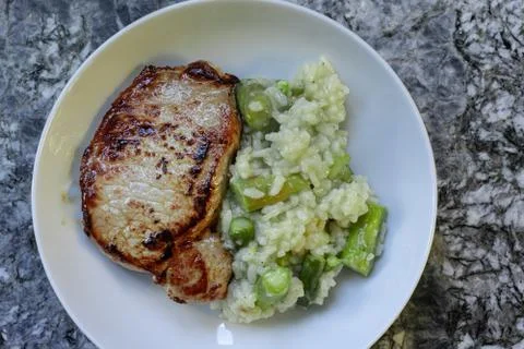 Roasted meat and risotto rice with asparagus in white round plate on granite Foto stock