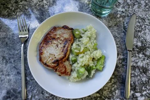 Roasted meat and risotto rice with asparagus in white round plate with fork a Stock Photos