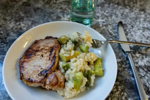 Roasted meat and risotto rice with asparagus in white round plate with fork a Stock Photos