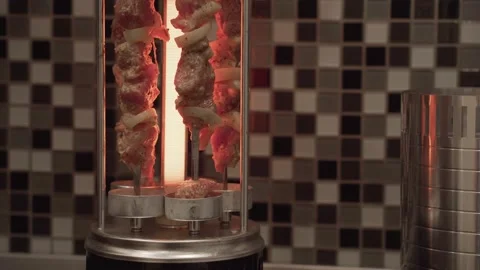 Roasted meat on a skewer rotates on a vertical barbecue grill. Kebab machine. Stock Footage 147415155