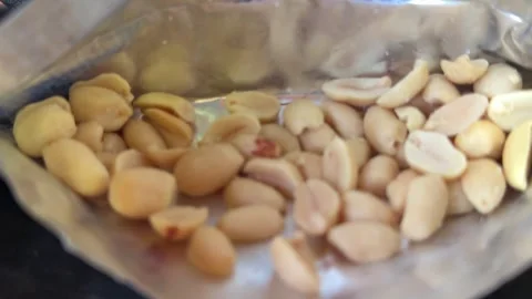 Roasted peanuts inside shiny foil package with handful of crunchy nuts and Stock Footage 345725825