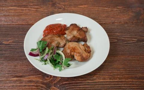 Roasted pork neck on a plate. Appetizing dish on the wooden brown table. Stock Photos