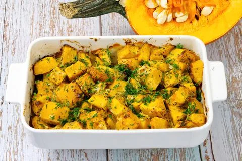 Roasted pumpkin in a ceramic pot on table with half raw squash Stock Photos