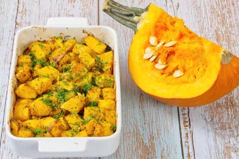 Roasted pumpkin in a ceramic pot on table with half raw squash Stock Photos