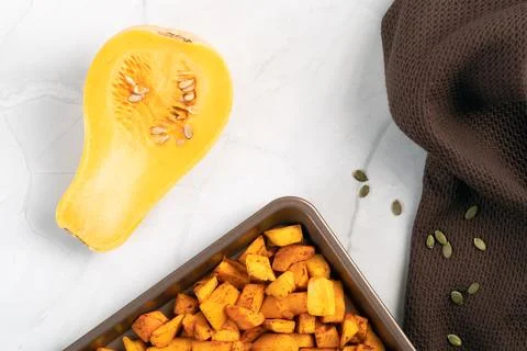 Roasted pumpkin cubes on baking tray with fresh halved squash Stock Photos