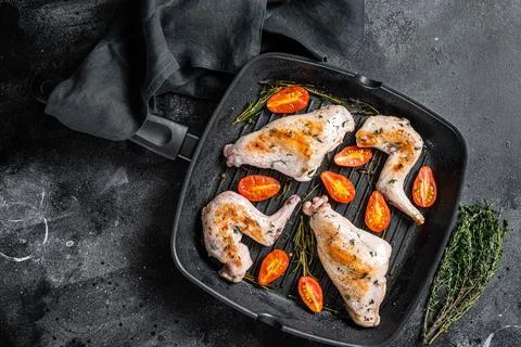Roasted rabbit legs in a pan with thyme. Black background. Top view Stock Photos
