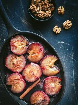Roasted red greengages on baking pan and walnuts in black bowl. Stock Photos