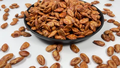 Roasted salted watermelon seeds in dark plate, white background Stock Footage 336847756