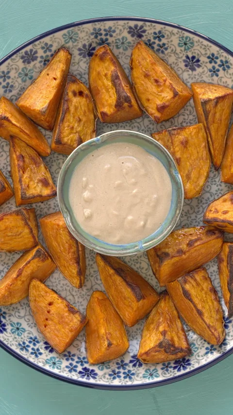 Roasted sweet potatoes, accompanied by a small bowl of tahini sauce. Stock Footage 325871228