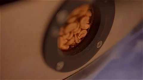 Roasting coffee .Coffee is mixed and fried in a roaster. view through a small Stock Footage 99750415