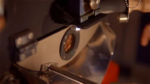 Roasting coffee .Coffee is mixed and fried in a roaster. view through a small Stock Footage 99750491
