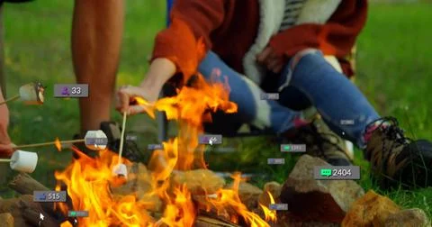 Roasting couple in rust jacket and hiking boots, holding marshmallows over Fotos Stock