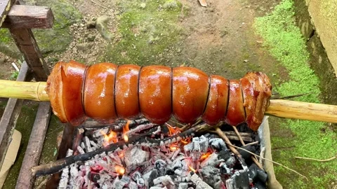 Roasting lechon belly on a bamboo spit over an open fire, a popular filipino Stock Footage 327907709