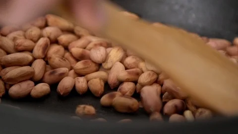 Roasting peanuts process. Mixing on skillet with wooden spatula close up Stock Footage 122516624