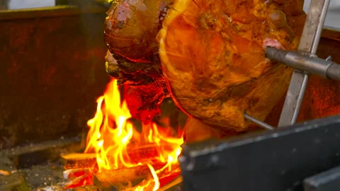 Roasting pork leg on spit over open fire at street market Stock Footage 334560645