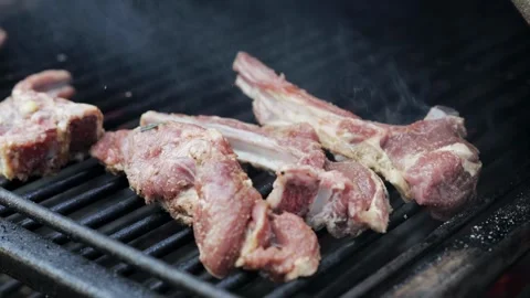 Roasting pork ribs on a grill grate in a barbecue oven, slow motion, close-up Stock Footage 323365497