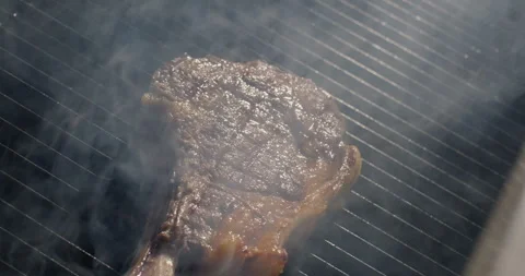 Roasting tomahawk steak on barbecue grid in smoke. Grilling BBQ meat. Close-up Stock Footage 277491116