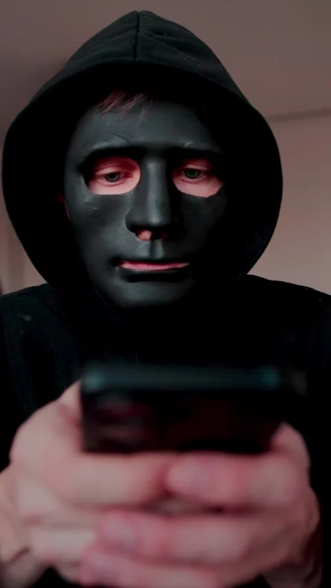 Robber in black mask using smartphone. Hacking, scamming. Vertical video. Stock Footage 329886098