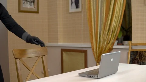 A robber is trying to hack into a laptop. A masked thug is sitting in a house Stock Footage 123733595