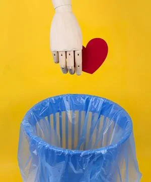 Robot hand dropping heart into trash bin on yellow background Stock Photos