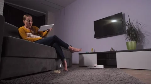 Robot hoover working while woman relaxing on sofa Stock Footage 145017595