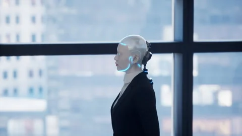 A robot humanoid staying in the empty office and looking out the window at the Stock Footage 256574540