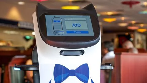 A robot with a large display screen and a charming blue bowtie stands in a mo Stock Photos