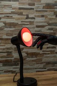 Robot or Prosthesis Hand Touching Glowing Smart Bulb in Desk Lamp Foto stock