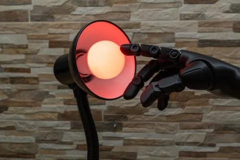 Robot or Prosthesis Hand Touching Glowing Smart Bulb in Desk Lamp Foto stock