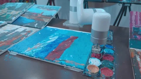 A robot painter at an exhibition dips a brush into paint and paints on a canvas Stock Footage 323916470