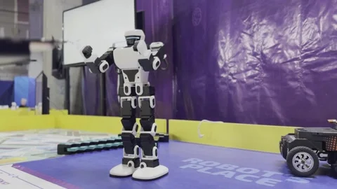 A robot is standing on a yellow mat in front of a purple wall Stock Footage 283486379