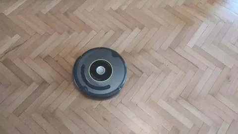 The robot vacuum cleaner cleans dirty wooden parquet floors in the living room Stock Footage 282259751